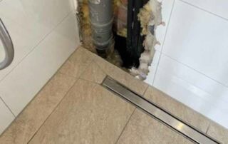 Reparatur einer Dusche. Durch eine Öffnung in den Wandfliesen ist ein Rohr zu sehen. SchadenDIENST24 ist Ihr Ihr kompetenter Partner für Haustechnik von Emlichheim bis Bad Bentheim, Lingen, Meppen und Umgebung.