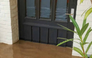 Eine Haustür, vor der der sehr hoch braunes Wasser steht. Der Boden ist nicht mehr zu sehen. Dieses Bild steht symbolisch für Hochwasser, das in Gebäude eindringt. SchadenDienst24 Nord-West hilft bei Hochwasser in Nordhorn, Lingen, Meppen, Emlichheim, Bad Bentheim und Umgebung.